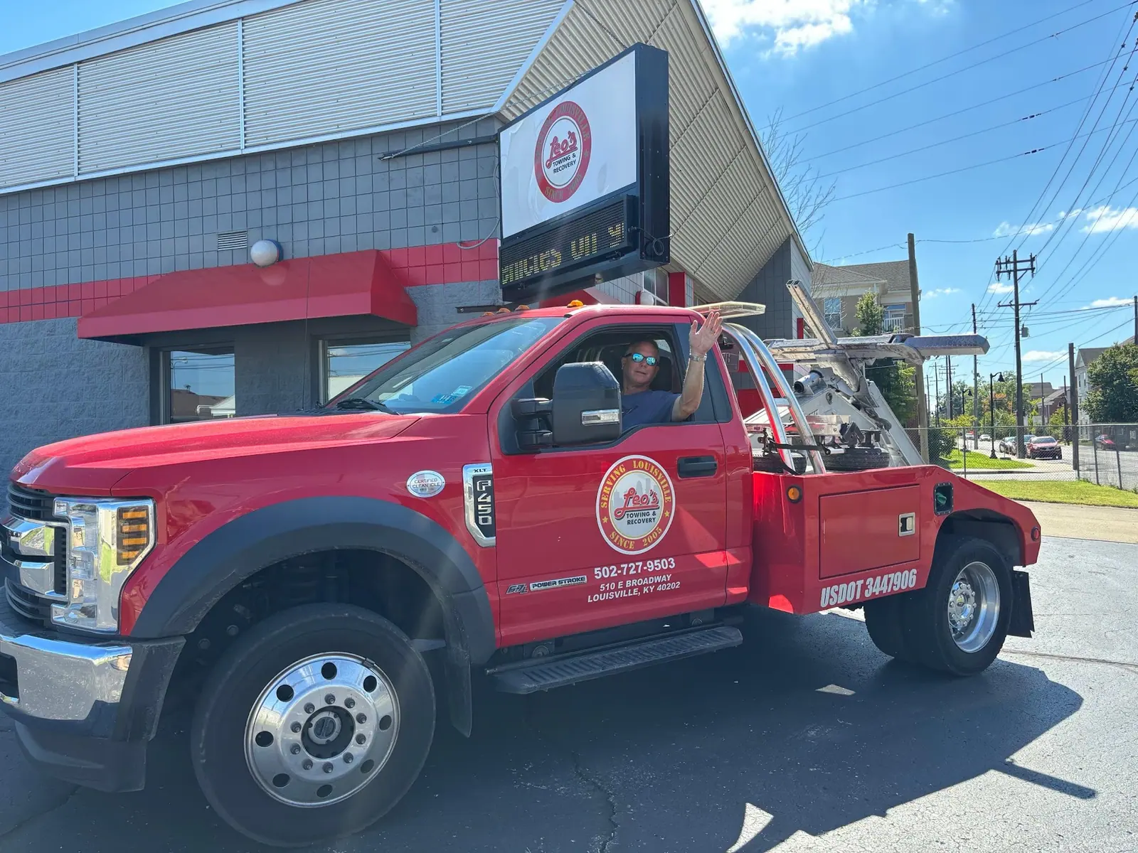 Leo's wrecker with its driver beside the storefront sign