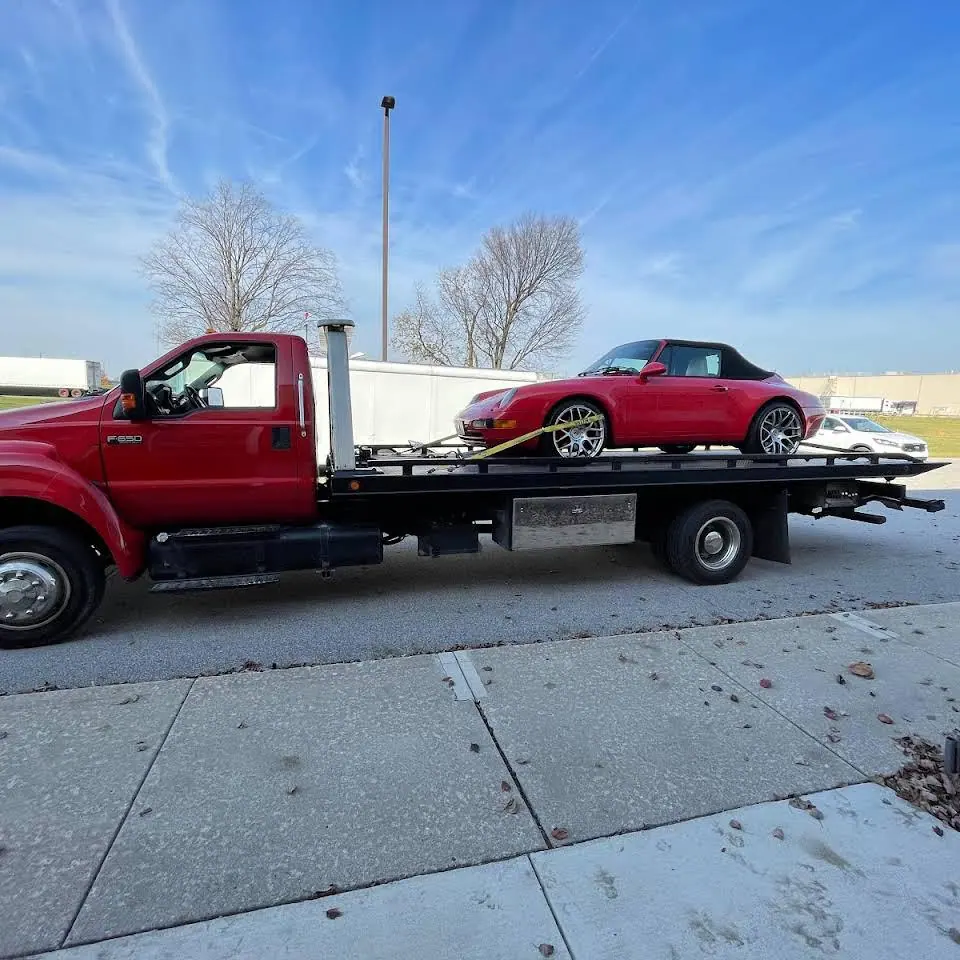Red flatbed with a red sports car loaded, parked by a sidewalk